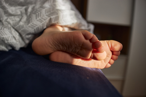 Close-up of a child's barefoot under cover peacefully sleeping in the bed.