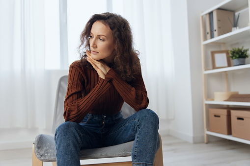 Heavy thoughts concept. Frustrated pensive thoughtful curly adorable woman reclines on hand lost in sad thoughts about irreparable mistake decision about abortion sit in chair at home looks aside