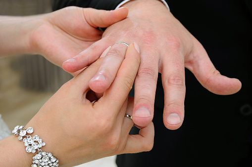 The bride puts on a white gold wedding ring for the groom in a close-up view from an angle