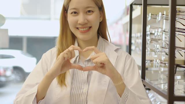 Attractive young female doctor use her hands to make a heart shape in eyeglasses shop, small new business startup or business owner.