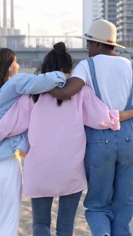 Rear view of three unrecognizable friends embracing each other while walking on the beach.