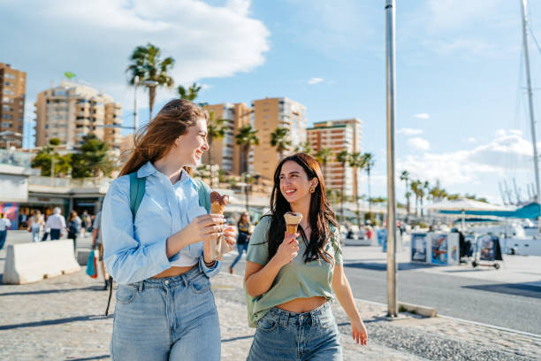Two Female Friends Eating An Ice Cream On The Quayside In Málaga In Spain Two beautiful female friends eating an ice cream while walking on the quayside in Málaga in Spain. málaga province stock pictures, royalty-free photos & images