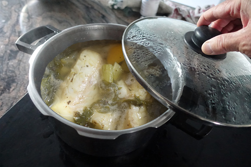 Cod being cooked in a spicy broth with condiments and aromatics