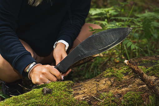 A girl holds a kukri sword in her hands outdoors in the forest for chopping wood. Close up photo