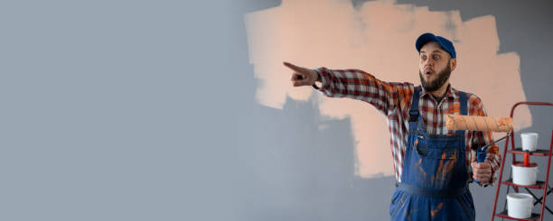 istock Painter man holding a paint roller surprised and pointing finger on advertising place 2147540087