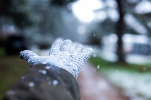 Unrecognizable hand in glove reaching for falling snowflakes, blurred forest backdrop eco-tourism