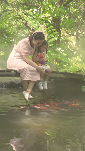Thai man's mother and daughter feeding koi fish as a family holiday activity.