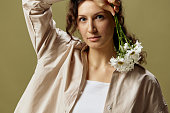Happy pretty lovely curly beautiful female in linen casual shirt hold chamomiles flowers near cheek posing isolated on over olive green pastel background. Nature is beauty concept. Copy space