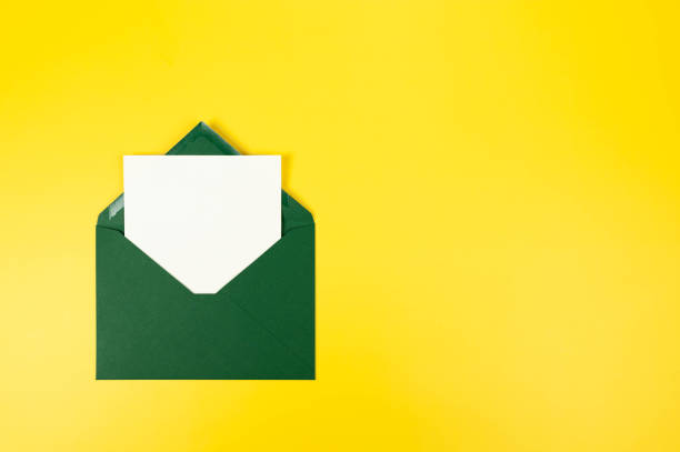 istock Top view of dark green envelope, white card on yellow background. 2147542990