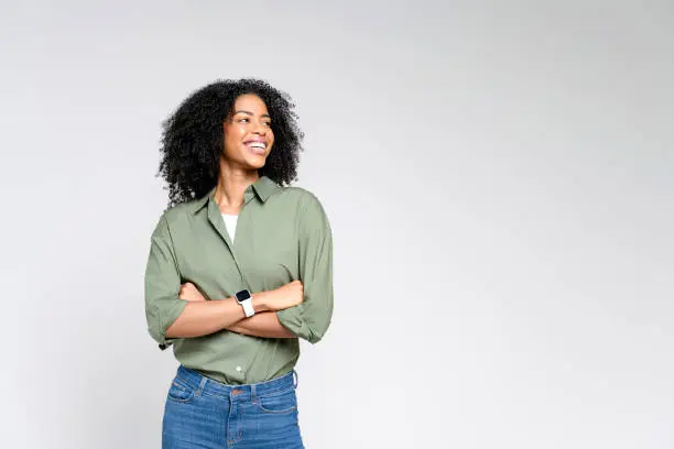 A confident African-American woman in a casual olive green shirt and jeans stands with a beaming smile A confident African-American woman in a casual olive green shirt and jeans stands with a beaming smile