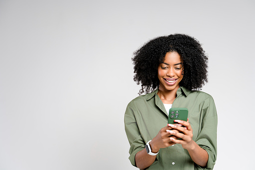 An African-American woman enjoys a moment on her smartphone, her contented smile reflecting the pleasure of digital connection. This modern shot encapsulates themes of communication and technology