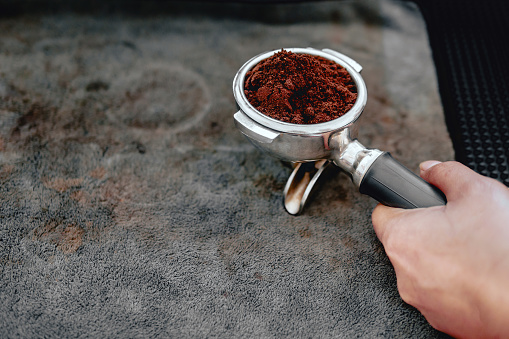 Equipment of coffee maker coffee portafilter filled with finely ground coffee In the hands of the barista getting ready to make coffee.