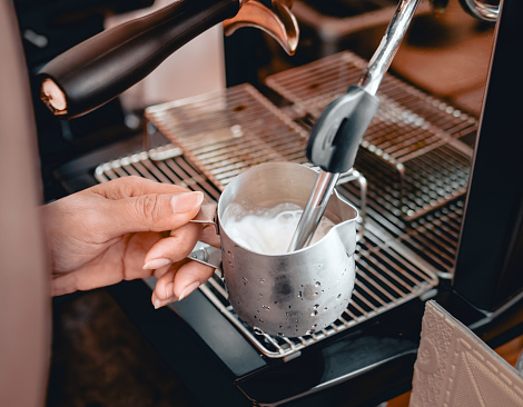 Close-up of Barista hand using high-pressure steam-operated milk frother to prepare a cappuccino and latte coffee milk