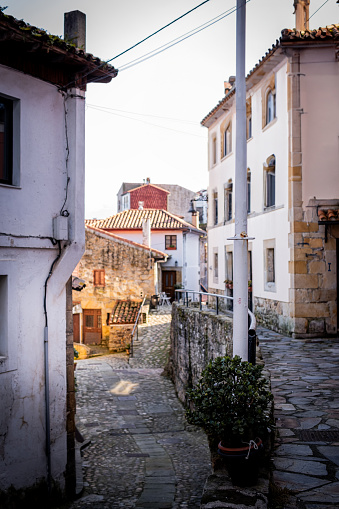 Stone pedestrian street in rural area, vibrant stone houses, warm tones, sunny Lastres.