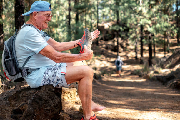 Carefree elderly man on a mountain hike stops to remove some pebbles from his shoe. Retired senior citizen enjoying a healthy lifestyle and freedom in nature.
