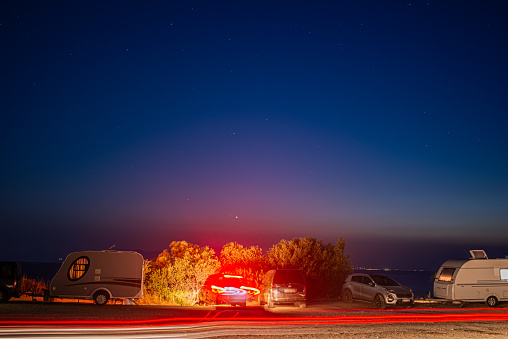 Mesmerizing long exposure capture of campers and vans at the coast, highlighting the serene beauty and shared moments of seaside camping under the starry sky.
