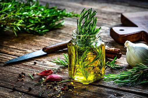 Olive oil, rosemary twigs, garlic and pepercorns on rustic table. High resolution 42Mp studio digital capture taken with Sony A7rII and Sony FE 90mm f2.8 macro G OSS lens
