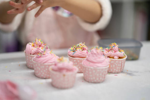 Little hands put colorful candies on a cupcake with pink whipped cream.