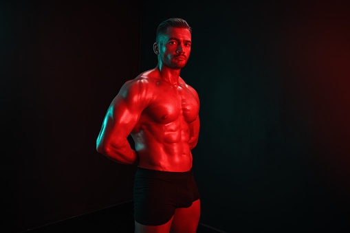 Man bodybuilder posing muscles with nude fitness torso, isolated on black background in neon light. Advertising, sports, active lifestyle, colored light, competition, challenge concept. . High quality photo