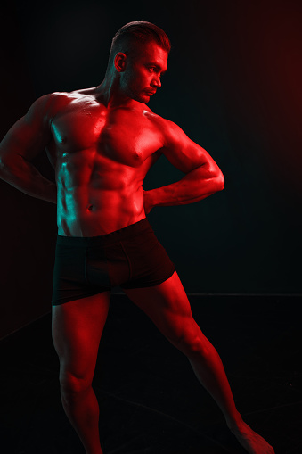 Man bodybuilder athlete with bare torso fashion pose on black isolated background with colored light neon red and green. The concept of a healthy male body sport. High quality photo