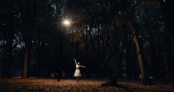 Ballet, dance and woman outdoor at night in Japan with street light, trees and creative art. Ballerina, performance and talent in dark Kyoto forest, woods or garden with spotlight