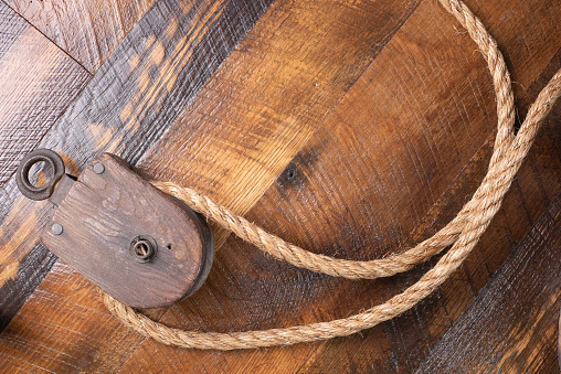 Antique block and tackle with jute rope on wooden background.