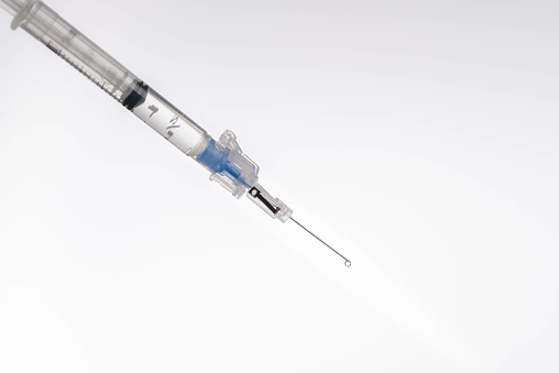 Medical syringe and needle with fluid dripping out of needle.