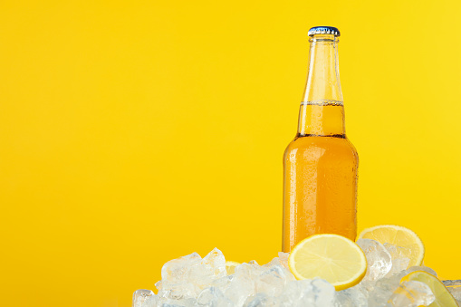 Bottle of drink in ice with lemon slices on yellow background