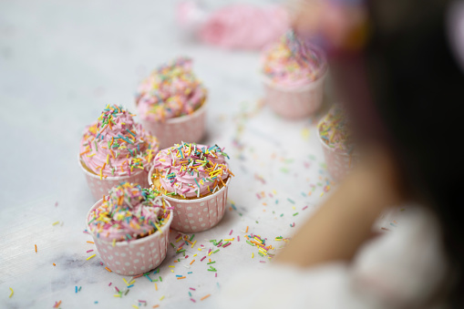 Little hands put colorful candies on a cupcake with pink whipped cream.