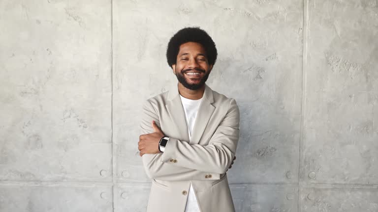 A confident smiling businessman stands arms crossed against a concrete backdrop