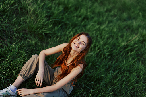 Happy woman smiling beautifully and looking up at the camera sitting on fresh green grass in the summer sunshine. High quality photo