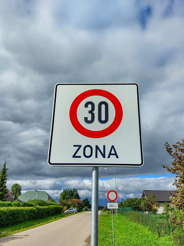 Metal road or traffic sign with number 30 in a red circle, and zone, indicating new speed limit against blue sky and clouds background