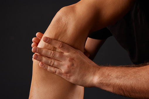 handsome male masseur doing a massage on a girl's leg on a black background, concept of therapeutic relaxing massage