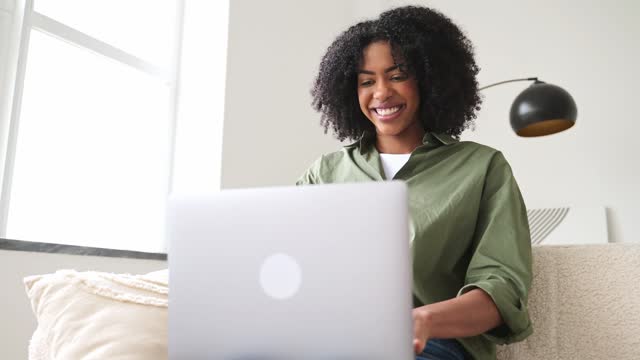 In a moment of joyful online interaction, an African-American woman smiles while working on laptop