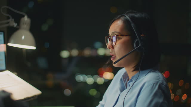 Young woman using a computer and headset at night in a modern office