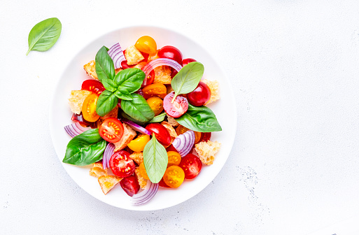 Summer italian salad with stale bread, tomatoes, red onion, olive oil, salt and green basil, white table background, top view