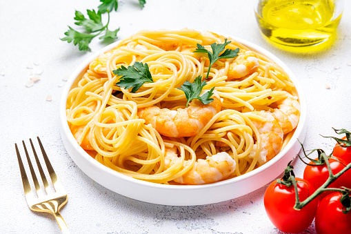 Delicious spaghetti pasta with big shrimp on plate with parsley, white table background. Top view