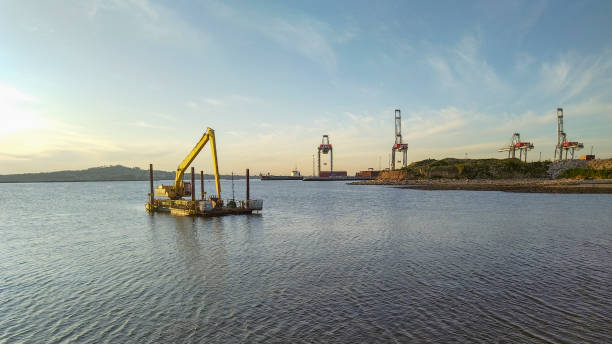 A white and yellow tug boat pulls a barge that in turn is pulling a dredge pipe toward the eastern end of the Cape Cod canal as a sand renourishment project is taking place.