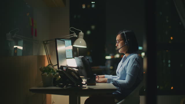 Young woman using a computer and headset at night in a modern office