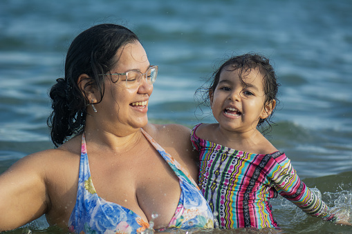 A girl and her mother are bathing in the sea and laughing, having fun. 
Loving mother playing with her little girl in the sea in summer