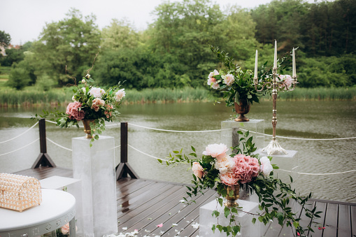 Beautiful round wedding arch decorated with flowers and greenery near lake or river outdoors, copy space. Decorations for wedding ceremony in open air. High quality photo