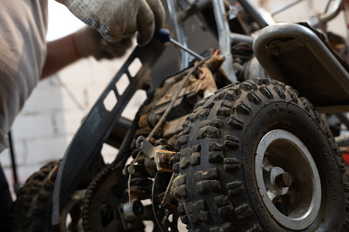 An ATV being repaired by an unqualified mechanic in a garage. A mechanic tightens a part on an ATV using a ratchet screwdriver. Replacing parts on a small ATV in your garage..