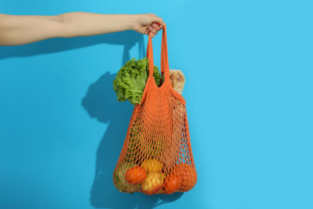 istock Female hand holds string bag with grocery on blue background 2147573257