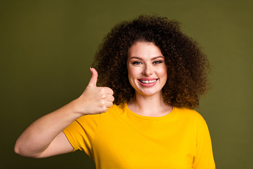 Retrato de una joven alegre con una camiseta amarilla que muestra el pulgar hacia arriba como símbolo de la comida de mcdonalds aislada sobre fondo de color caqui photo