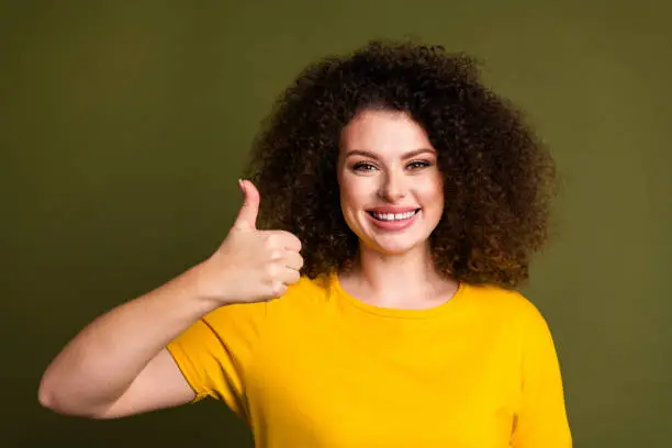 Portrait of young cheerful lady wearing yellow t shirt showing thumb up like symbol mcdonalds food isolated on khaki color background.