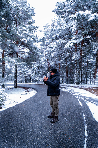 Vertical wide-angle landscape, latino Peruvian youth in mountain gear takes mobile photo of snowfall