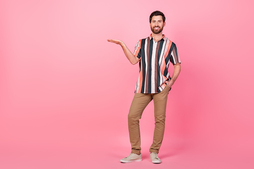 Full length body size photo of young man striped t shirt and pants promoting upgraded marketing strategy isolated on pink color background.