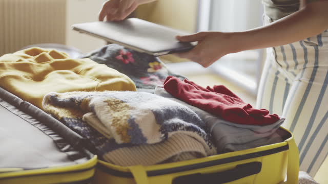 Young girl getting ready for travel, packing clothes and laptop in a yellow suitcase. Concept of traveling, adventure. lady with a beautiful tattoo collects the most necessary things before the trip.