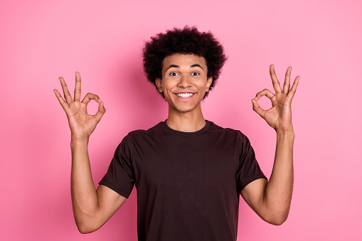 Photo of toothy beaming hollywood smile young guy in brown t shirt show double okey symbol feedback isolated on pink color background.