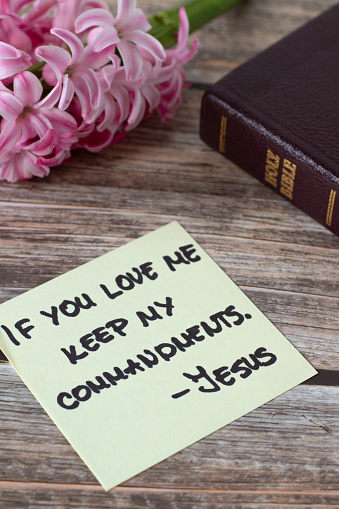 If you love Me keep My commandments, Jesus Christ, handwritten quote with holy bible book and flower on wood. Close-up. Christian obedience to God, 10 commandments, biblical concept.